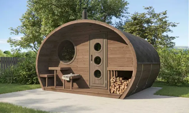 Fasssauna aus thermisch modifiziertem Holz mit runden Fenstern und Holzstapel.