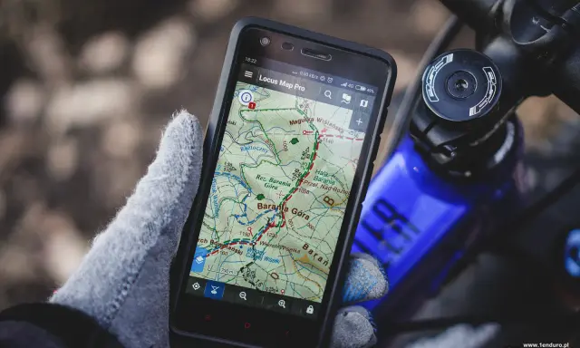 Rękawiczka trzyma smartfon z mapą górską, pokazującą darmowa aplikacja na rower. Idealna do nawigacji w terenie.