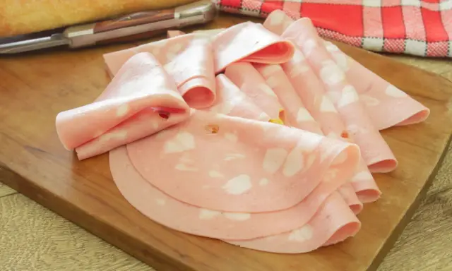 Fette di salame rosa, come in attesa di un lieto evento, disposte su un tagliere di legno.