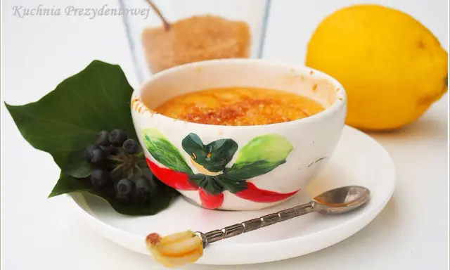 Słodka, karmelizowana crema catalana w ozdobnej miseczce, obok cytryna i jagody.