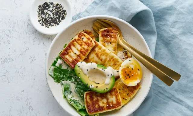 Szybki keto obiad: grillowany ser halloumi, awokado, jajko na miękko i zielone liście, posypane sezamem.