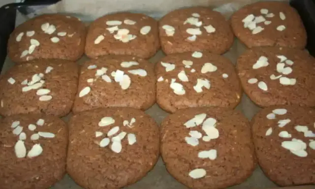 Douze biscuits faits maison, parfaits pour une recette speculoos, garnis d'amandes effilées sur une plaque de cuisson.