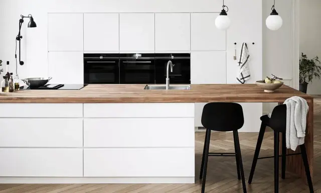 Un plan de travail en bois chaleureux contraste avec les meubles de cuisine blancs. Quelle couleur de plan de travail pour une cuisine blanche ? Le bois est une option parfaite.