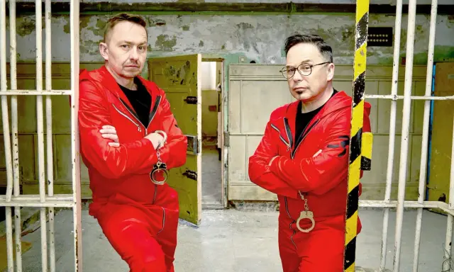Dwóch mężczyzn w czerwonych kombinezonach i kajdankach, gotowych do ucieczki. Czy uda im się unlock po polsku?