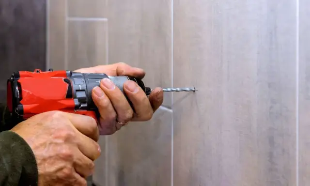Man usa una broca para azulejo con un taladro para hacer un agujero en una pared de azulejos.