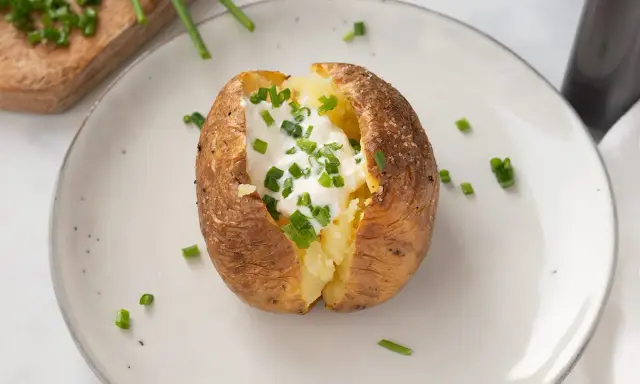 Patatas asadas en freidora de aire, crujientes por fuera, tiernas por dentro, coronadas con crema agria y cebollino fresco.