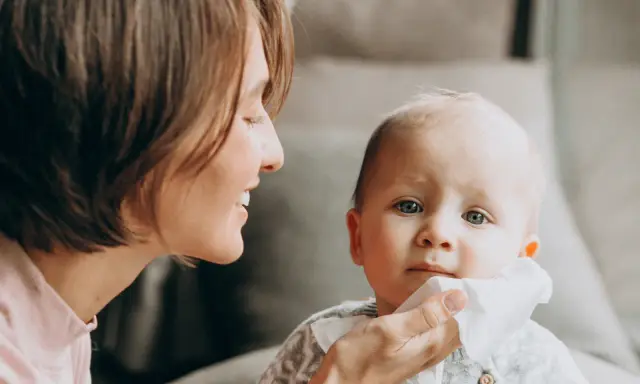 Mama delikatnie wyciera buzię dziecka, które ma żółty katar.