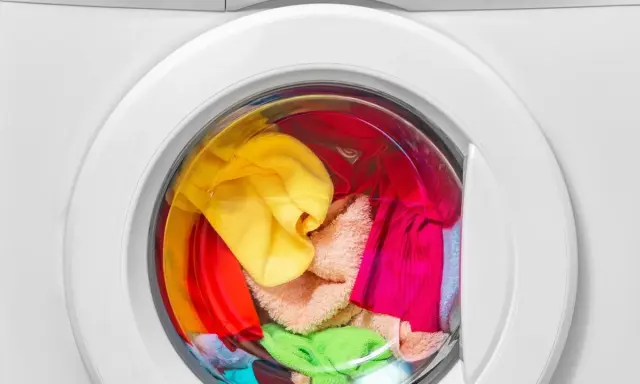 Bunte Wäsche, darunter ein gelber und ein grüner Schwamm, wartet in der Waschmaschine auf das schwamm waschen.