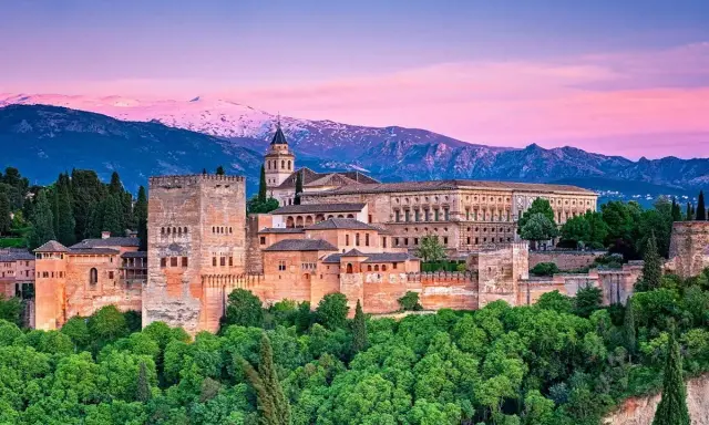 Alhambra w Granadzie na tle ośnieżonych gór i różowego nieba o zachodzie słońca.