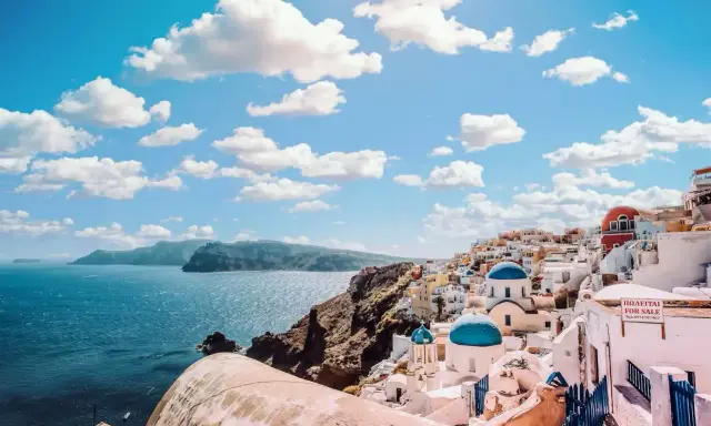 Santorini, Grecja. Białe domy z niebieskimi kopułami kościołów na zboczu góry, nad turkusowym morzem. Marzysz o podróży? Sprawdź, ile się leci do Grecji!