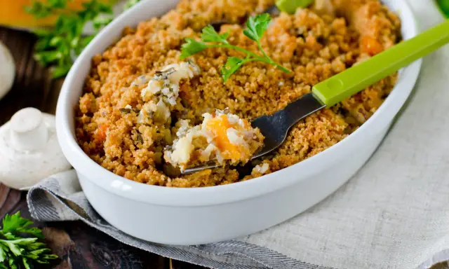 Un délicieux crumble salé aux légumes et riz, servi dans un plat blanc, avec une fourchette verte prête à déguster.