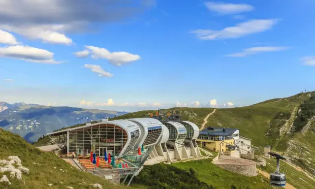 Moderne Seilbahnstation am Monte Baldo mit Panoramablick auf die Berge. Eine Gondel fährt den Hang hinauf.