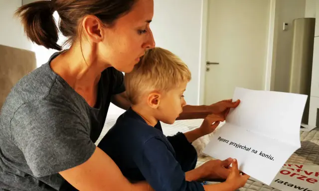 Mama pomaga synkowi w nauce czytania. Razem czytają zdanie "Rycerz przyjechał na koniu".