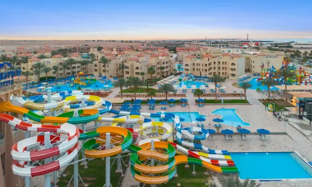 Kolorowe zjeżdżalnie wodne i baseny w Albatros Aqua Park, otoczone palmami i hotelami, zapraszają do zabawy.