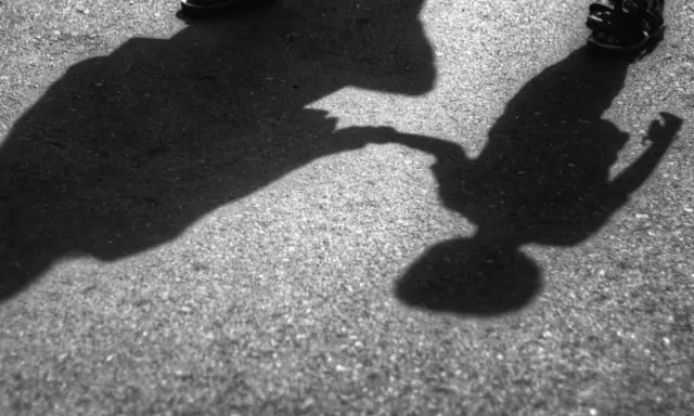 Dwie postacie, dorosła i dziecko, trzymają się za ręce. Cienie na asfalcie sugerują, że to może być dowód na reinkarnację, gdzie dusze odnajdują się w kolejnych wcieleniach.