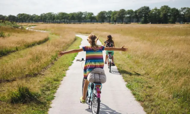Zwei Mädchen genießen eine Fahrradtour in NRW auf einem Feldweg, umgeben von goldenem Gras und Bäumen.