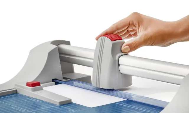 Mano operando una guillotina o cizalla para cortar papel con precisión.