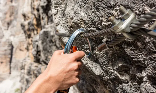 Dłoń zapina karabinek do stalowej liny na via ferrata. Bezpieczeństwo podczas wspinaczki.
