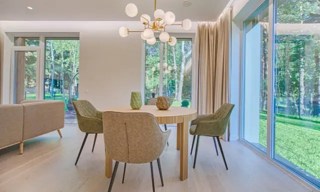 Éclairage salle à manger sans plafonnier : suspension moderne au-dessus d'une table ronde, entourée de chaises vertes. Lumière naturelle abondante des grandes fenêtres.