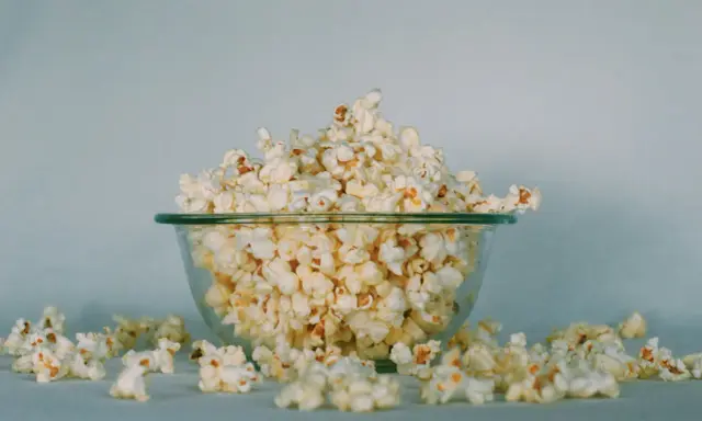Góra popcornu w szklanej misce, rozsypane ziarna wokół. Ile popcorn kcal?