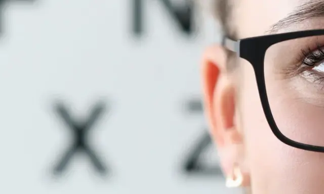 Po operacji zaćmy, czy po operacji zaćmy trzeba nosić okulary przeciwsłoneczne? Oko w okularach na tle tablicy Snellena.