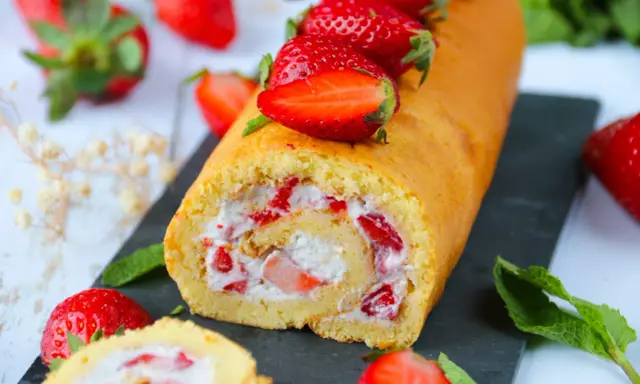 Un roulé aux fraises moelleux, garni de crème et de morceaux de fraises fraîches, décoré de fraises entières.