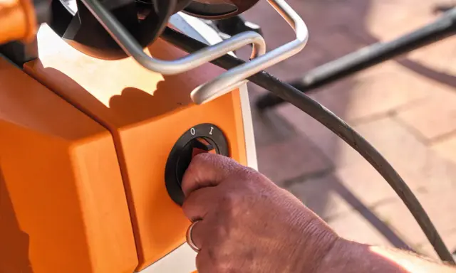 Hand dreht Schalter am orangefarbenen Hochdruckreiniger. Vorbereitung zum Anschluss an den Wasserhahn.