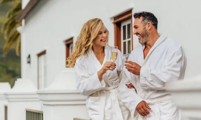 Para relaksu w hotelach spa w Polsce. Uśmiechnięta para w szlafrokach wznosi toasty szampanem na balkonie.