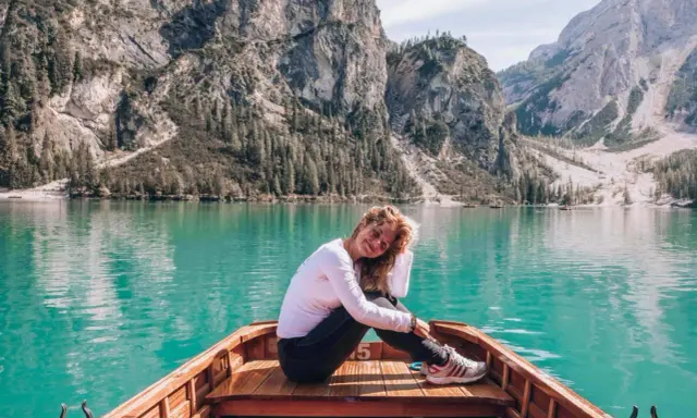 Kobieta w łodzi na turkusowym jeziorze w Dolomitach, w tle góry i las.