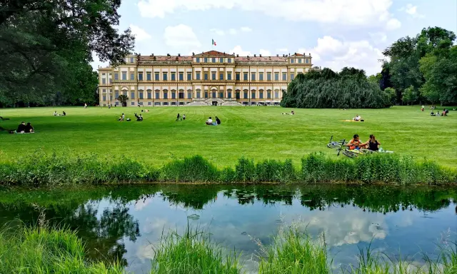 Villa Reale di Monza e il suo parco: un'idea per cosa vedere a Monza in un giorno. Persone rilassate sull'erba, un laghetto e il maestoso edificio.