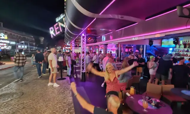 Nachts auf der Albufeira Partymeile: Menschen tanzen und feiern unter Neonlicht in Bars und Clubs.