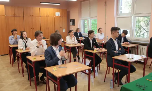 Uczniowie siedzą w ławkach podczas egzaminu. Zastanawiają się, ile trwa matura z biologii, skupieni na zadaniach.