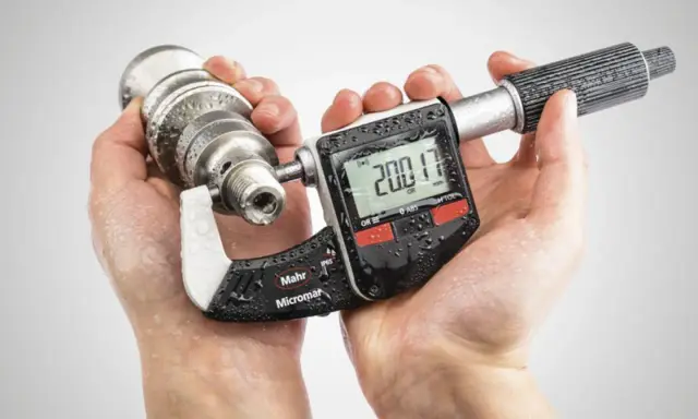 Manos sostienen un micrometro digital Mahr Micromar, midiendo una pieza metálica. La pantalla muestra 200.17 mm.