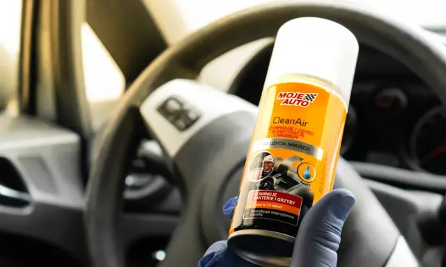 Rękawiczka w niebieskiej rękawiczce trzyma puszkę Moje Auto CleanAir do czyszczenia klimatyzacji.