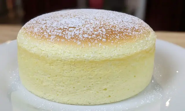 Un délicieux cheesecake japonais, léger et aérien, saupoudré de sucre glace sur une assiette blanche.