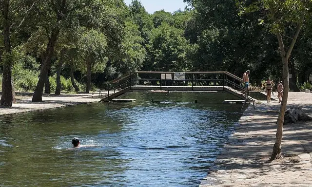 Un día soleado en las piscinas naturales de La Codosera. Personas disfrutan del agua fresca, una nada mientras otras pasean por la orilla.