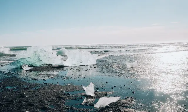Lodowe bryły lśnią na czarnym piasku, tworząc magiczny diamond beach. Fale obmywają brzeg, a słońce odbija się w wodzie.