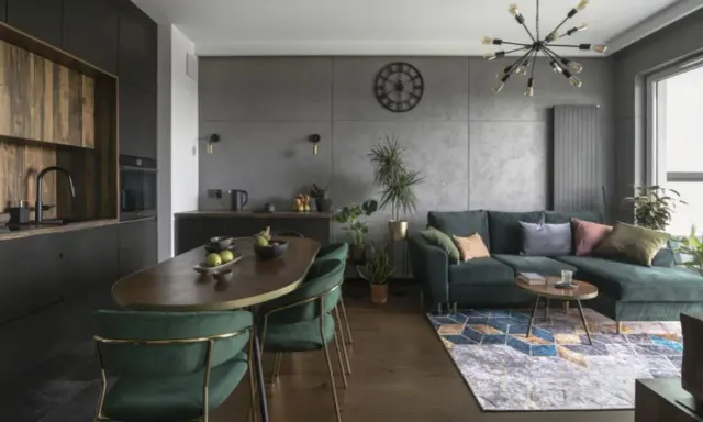 Nowoczesny czarny salon z drewnem, zielona kanapa, owalny stół i designerska lampa.