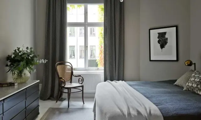 Sovrum med en säng, en stol och en byrå. Konst av Sofia Wallenstam på väggen.