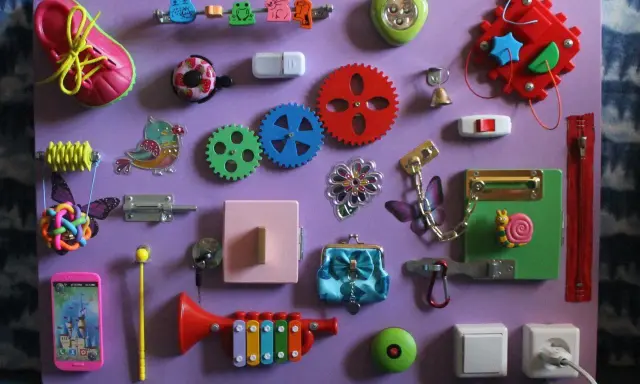 Lavagna sensoriale fai da te con scarpa, ingranaggi, campanello, lucchetto e altri elementi per stimolare i bambini. Perfetta per giochi montessori 2 anni fai da te.