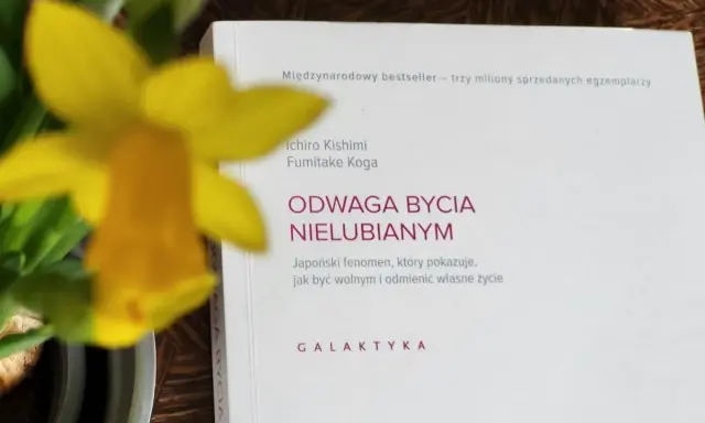 Żółty narcyz obok książki "Odwaga bycia nielubianym". Odkryj sztukę bycia sobą i wolności.