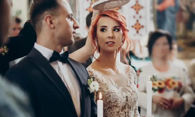 Para młoda podczas ceremonii ślubnej. Panna młoda w koronkowej sukni i pan młody w garniturze, trzymają świece.