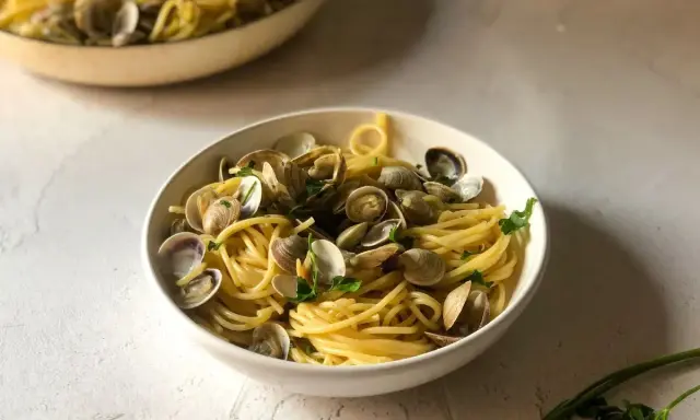 Un invitante piatto di spaghetti alle vongole, con pasta dorata e molluschi freschi, guarnito con prezzemolo.
