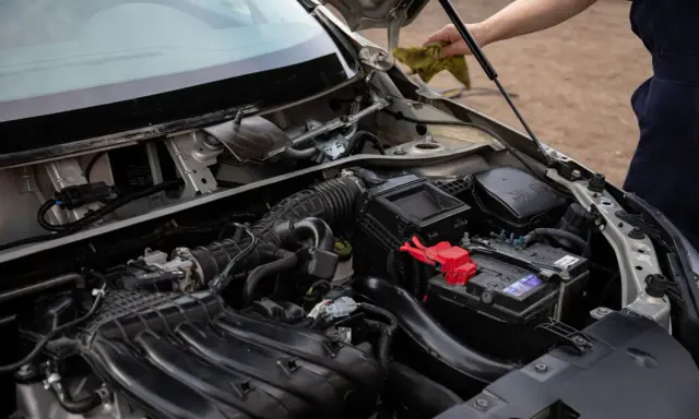 Silnik samochodu z widocznym akumulatorem i elementami układu dolotowego. Czy to zepsuty alternator czy akumulator?