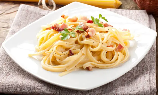 Pyszny makaron carbonara z boczkiem i natką pietruszki na białym talerzu.