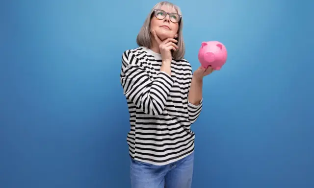 Mujer pensativa con hucha rosa, considerando los tipos de planes de pensiones para su futuro.