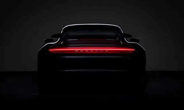 Ein schwarzer Porsche von hinten, dessen Rückleuchten in einem leuchtenden Rot erstrahlen und den Schriftzug "PORSCHE" beleuchten.