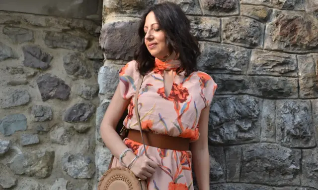 Donna con abito floreale rosa antico, cinturone marrone e borsa rotonda. I colori vivaci del vestito sono perfetti per abbinare al rosa antico.