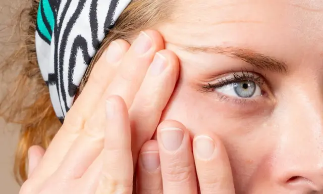 Doigts appliquant un soin pour le massage cernes, près d'un œil bleu. Bandeau à rayures zébrées.