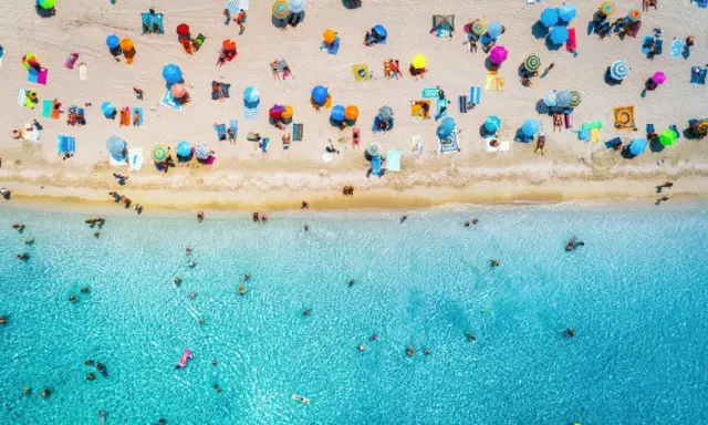 Un'affollata spiaggia di Rimini mare, con ombrelloni colorati e bagnanti che si godono il sole e il mare cristallino.